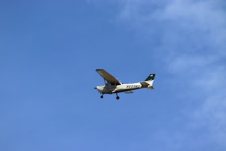 A small propeller airplane is flying against a clear blue sky. The aircraft has a distinctive tail number visible on its side.
