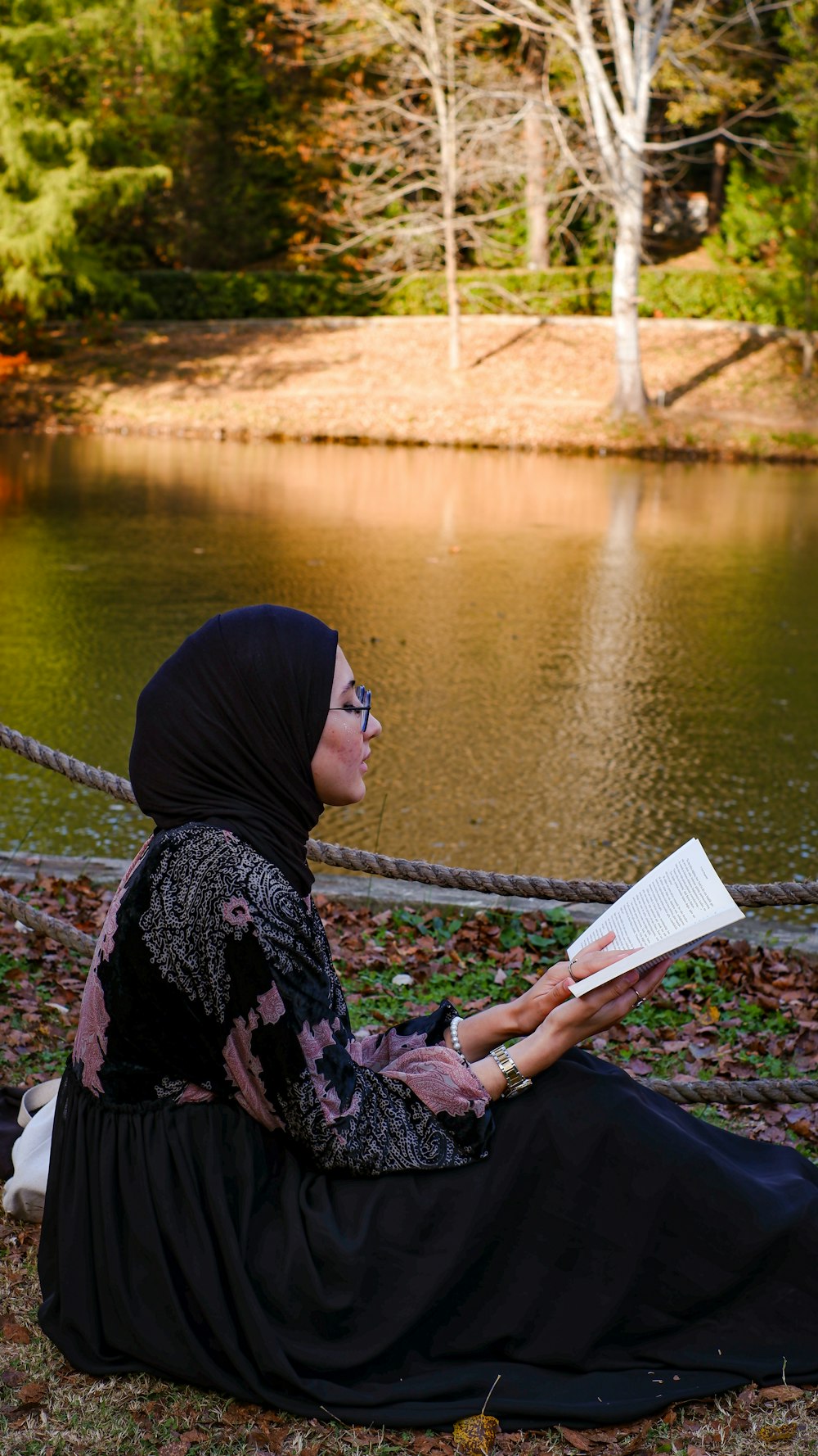 a person sitting on the ground reading a book by a lake
