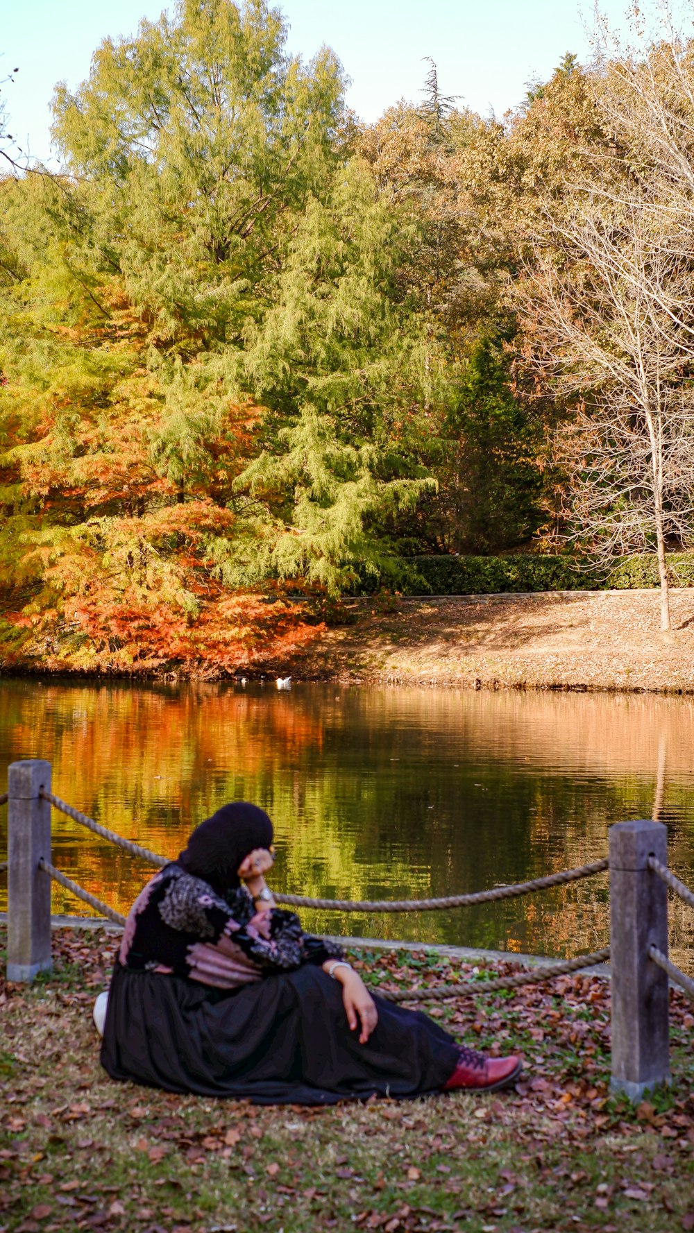 uma pessoa sentada em um cobertor à beira de um lago com árvores ao fundo
