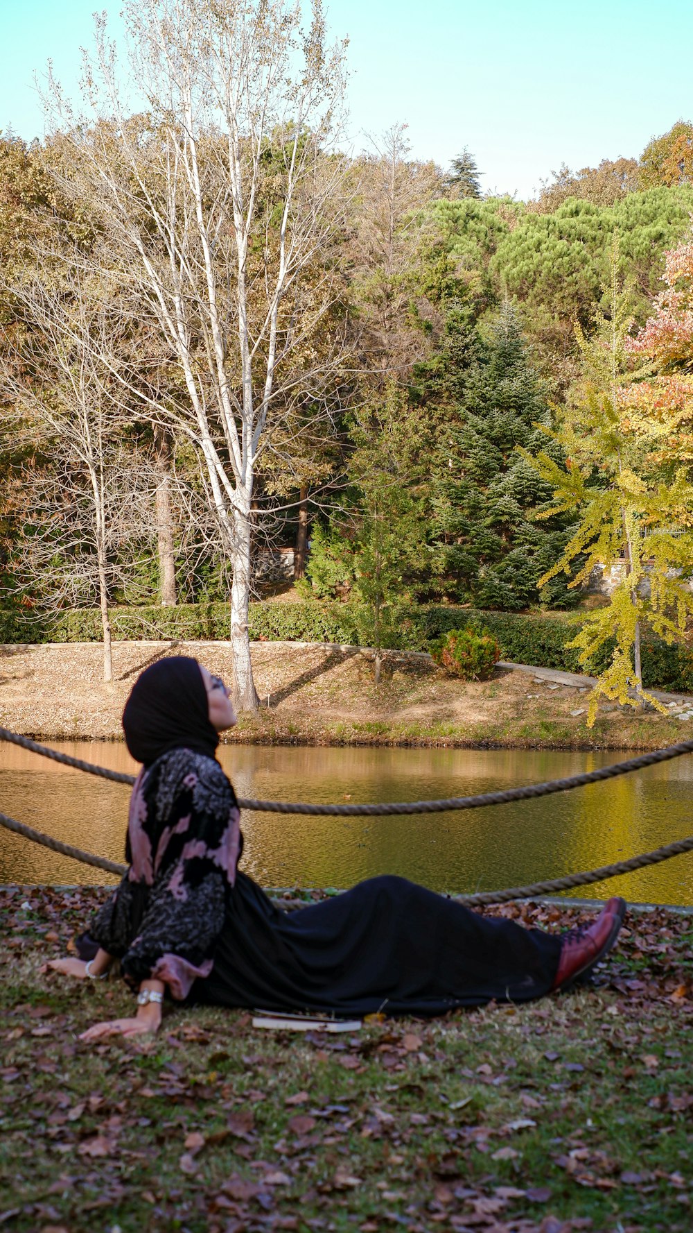a person sitting on a bench by a pond with trees