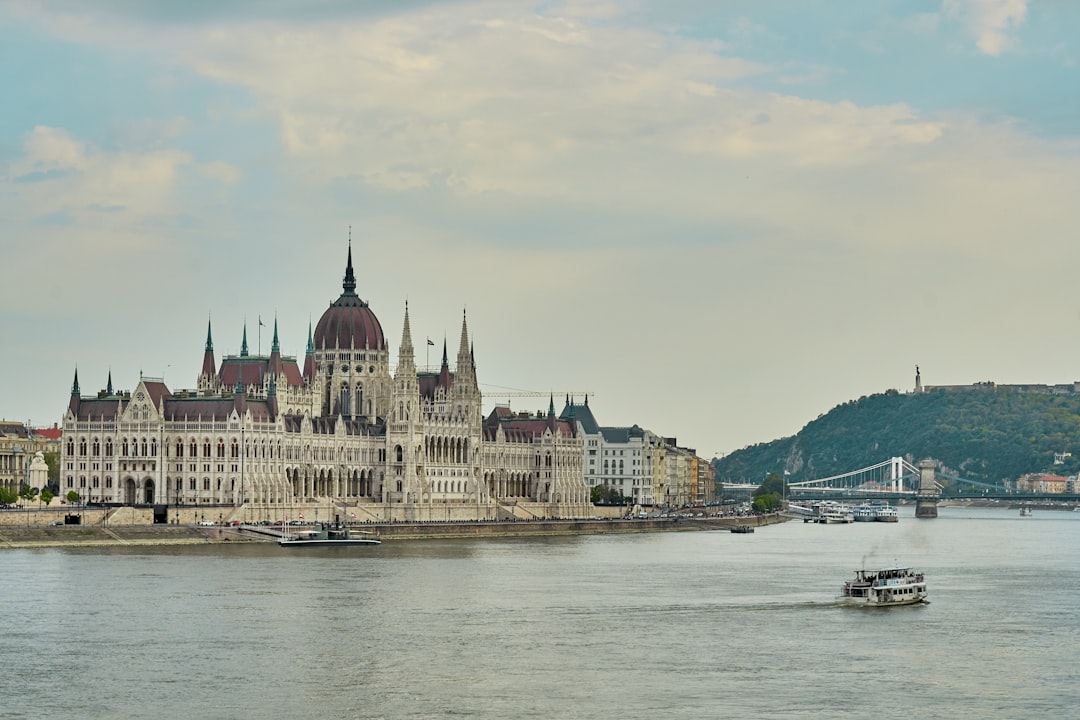 a large building with towers by a body of water with Hungarian Parliament Building in the background,