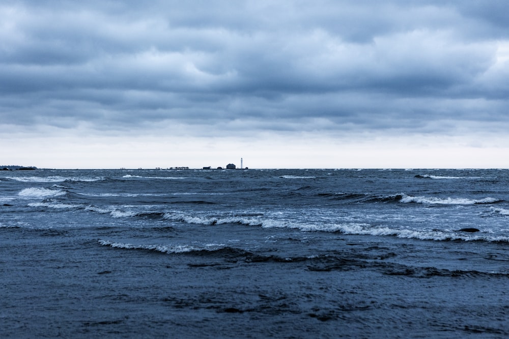 a beach with waves and a lighthouse in the distance