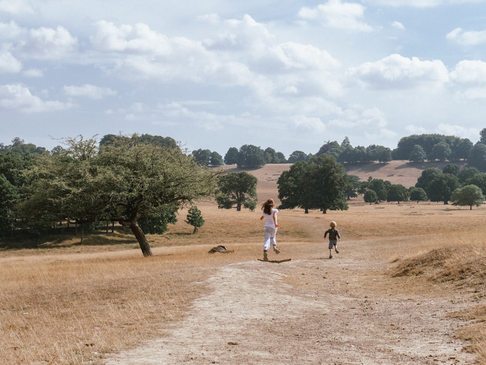 a couple of people walking on a dirt road with trees and grass