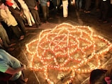A group of smiling people lighting dhoop cones together in a sunlit courtyard.