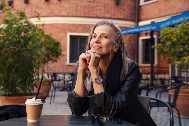 Woman with grey hair at a café, resting her chin on her hands
