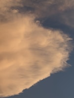 A large, fluffy cloud dominates the upper portion of the image, with a soft, creamy white color against a deeper blue sky. The edges of the cloud are wispy and diffuse, blending into the sky.