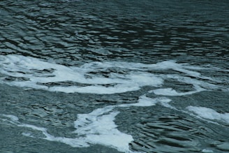 Dark water with white foam patterns intertwining on the surface, creating a textured and wavy effect.
