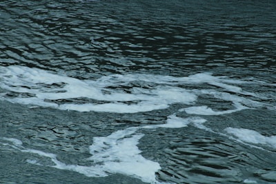 Dark water with white foam patterns intertwining on the surface, creating a textured and wavy effect.