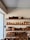 A set of wooden shelves displays a variety of neatly stacked wooden kitchenware, including bowls, plates, trays, and cutlery. The items are carefully organized, and the shelves are placed against a light-colored wall, adjacent to a window that lets in natural light.