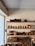 A set of wooden shelves displays a variety of neatly stacked wooden kitchenware, including bowls, plates, trays, and cutlery. The items are carefully organized, and the shelves are placed against a light-colored wall, adjacent to a window that lets in natural light.