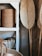 Several woven baskets are arranged on a white wooden shelf. The baskets display intricate patterns and are made from natural materials. Tall woven fans or paddles lean against the wall, complementing the earthy tones of the scene.