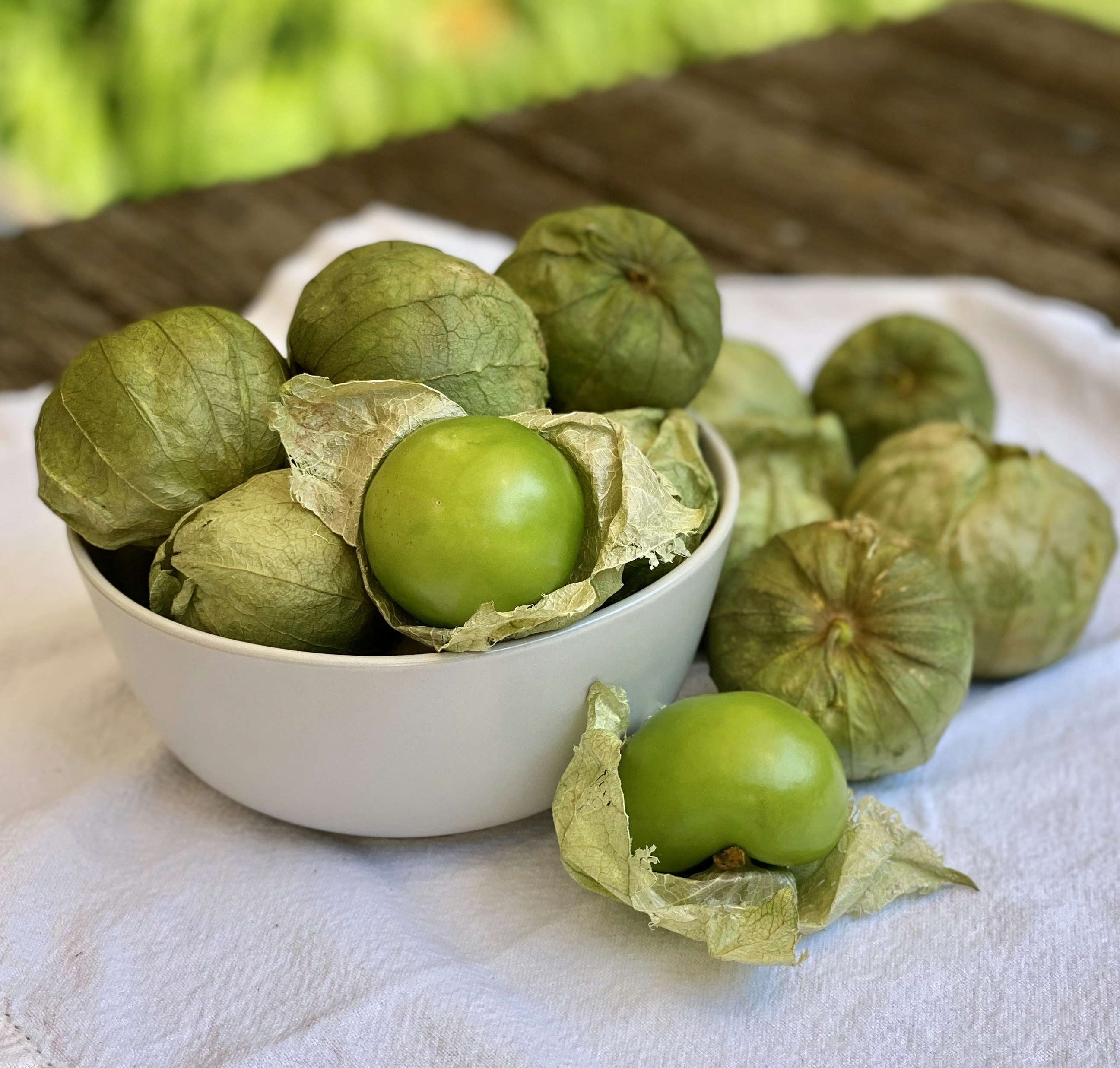 Fresh green tomatillos with husks in a white bowl`