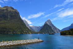 a body of water with boats and mountains in the background with Milford Sound in the background
