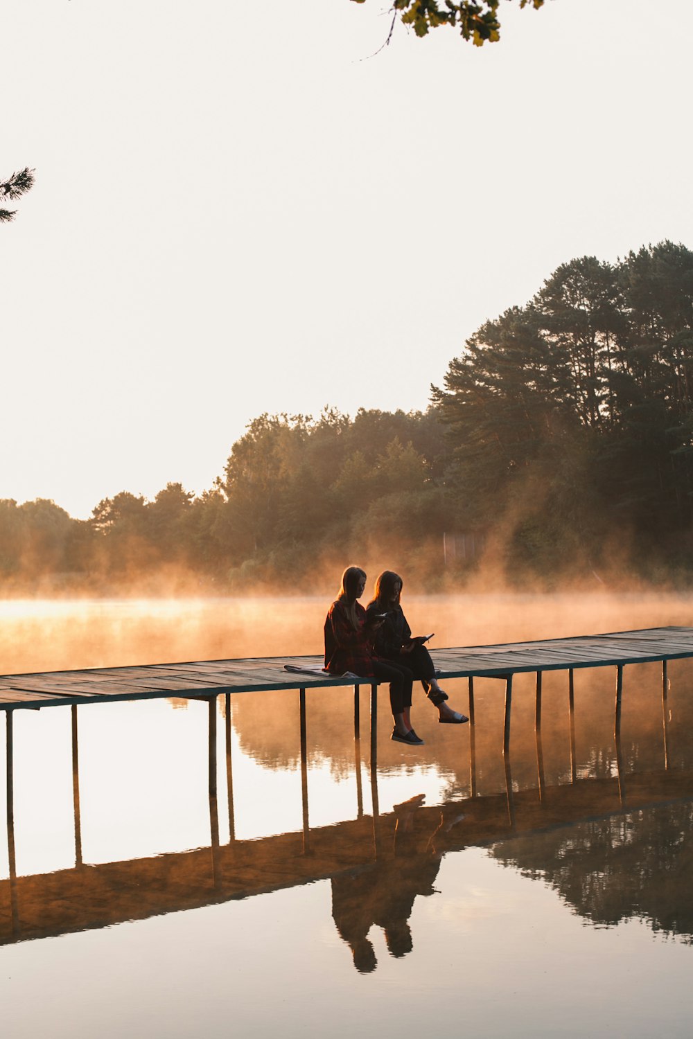 a man and woman sitting on a dock by a lake