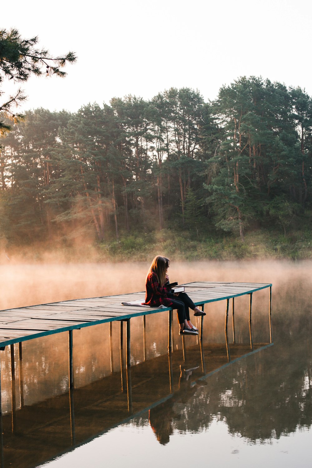 a person sitting on a dock by a body of water with trees in the background