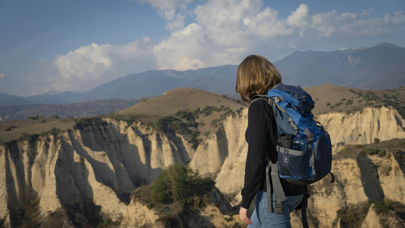Solo traveler with a backpack standing alone at a viewpoint, facing an open landscape, a decision-framing scene for taking a gap year