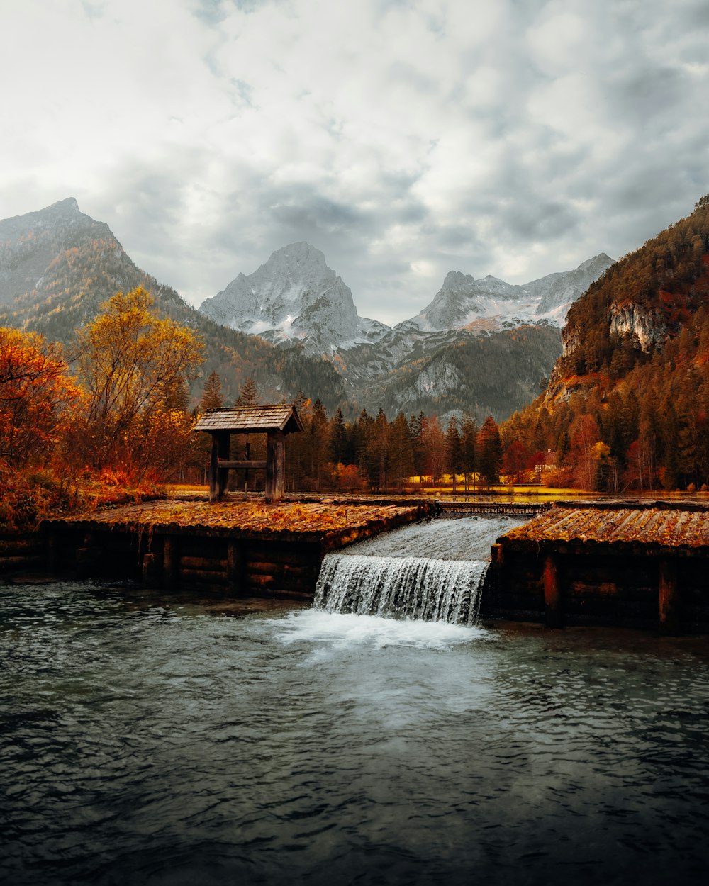 a small building on a bridge over a river with mountains in the background
