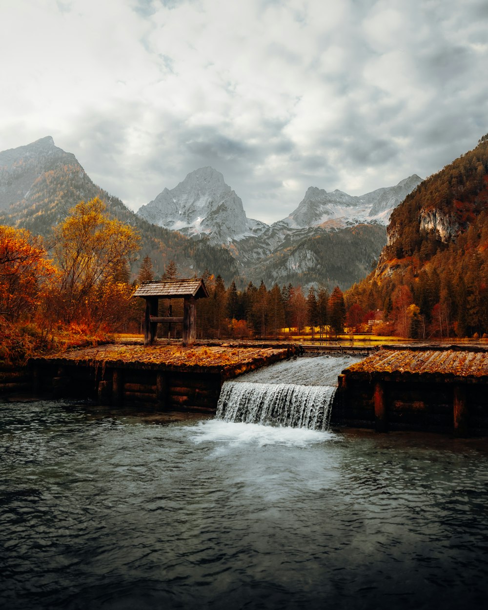 un petit bâtiment sur un pont au-dessus d’une rivière avec des montagnes en arrière-plan