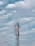 A tall communication tower with antennas and a satellite dish is set against a backdrop of a partly cloudy sky. The structure is composed of metal frameworks and various technological components.