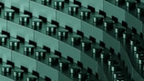 A close-up view of interconnected dark green building blocks with cylindrical connectors, arranged in diagonal rows, creating a repetitive and geometric pattern.