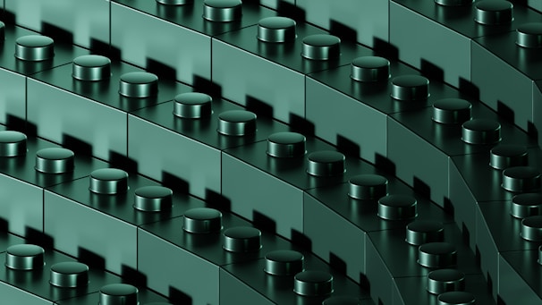 A close-up view of interconnected dark green building blocks with cylindrical connectors, arranged in diagonal rows, creating a repetitive and geometric pattern.