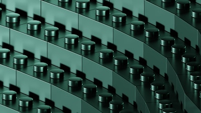 A close-up view of interconnected dark green building blocks with cylindrical connectors, arranged in diagonal rows, creating a repetitive and geometric pattern.