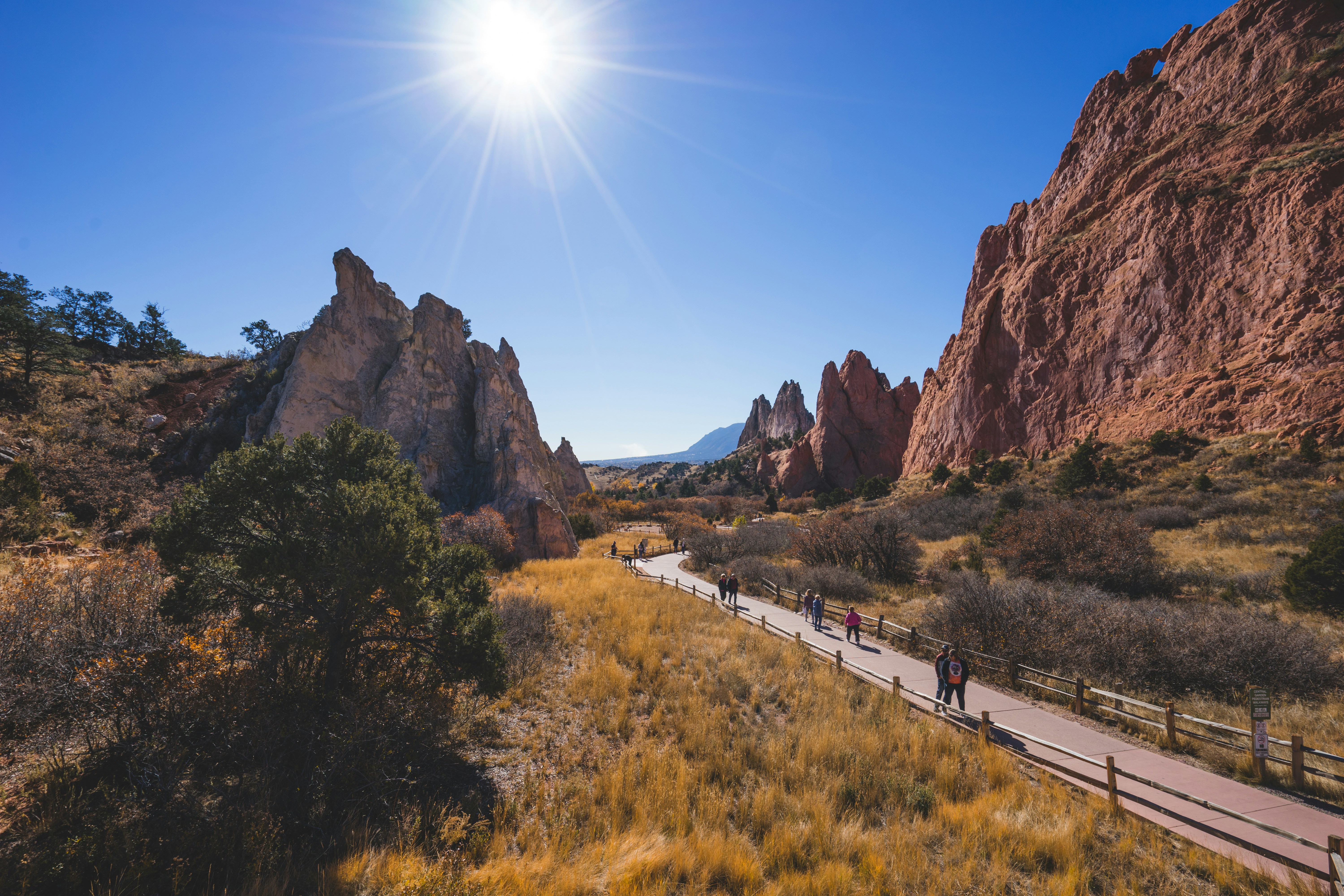 Hikers walk along a trail between tall red sandstone rocks.