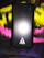A black rectangular electronic device, likely a power bank, with the logo 'iVOOMi' printed on it. The device is placed on a multicolored fabric background with shades of yellow, pink, and purple. There are small blue indicator lights on the upper right corner of the device.
