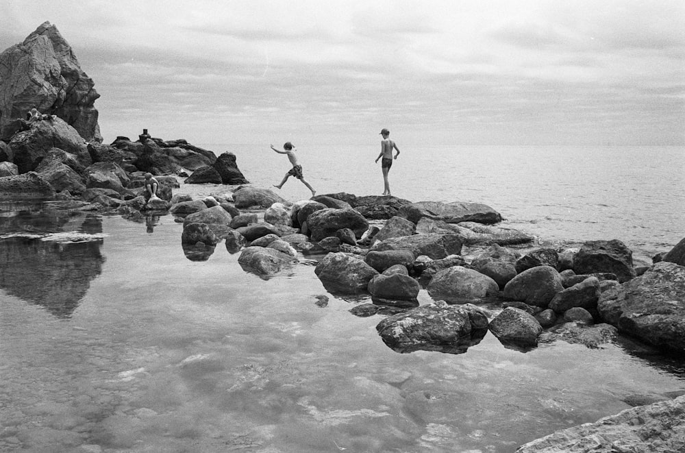 a couple of people standing on rocks by a body of water