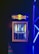 A compact beverage fridge with a transparent door filled with various cans of energy drinks. The fridge has a prominent logo on top featuring two red bulls and a yellow sun. The scene is lit with blue lighting, creating a vibrant and dynamic atmosphere.