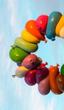 A vibrant, large balloon arch set up outdoors in a sunny park, filled with colorful balloons in various shapes and sizes.