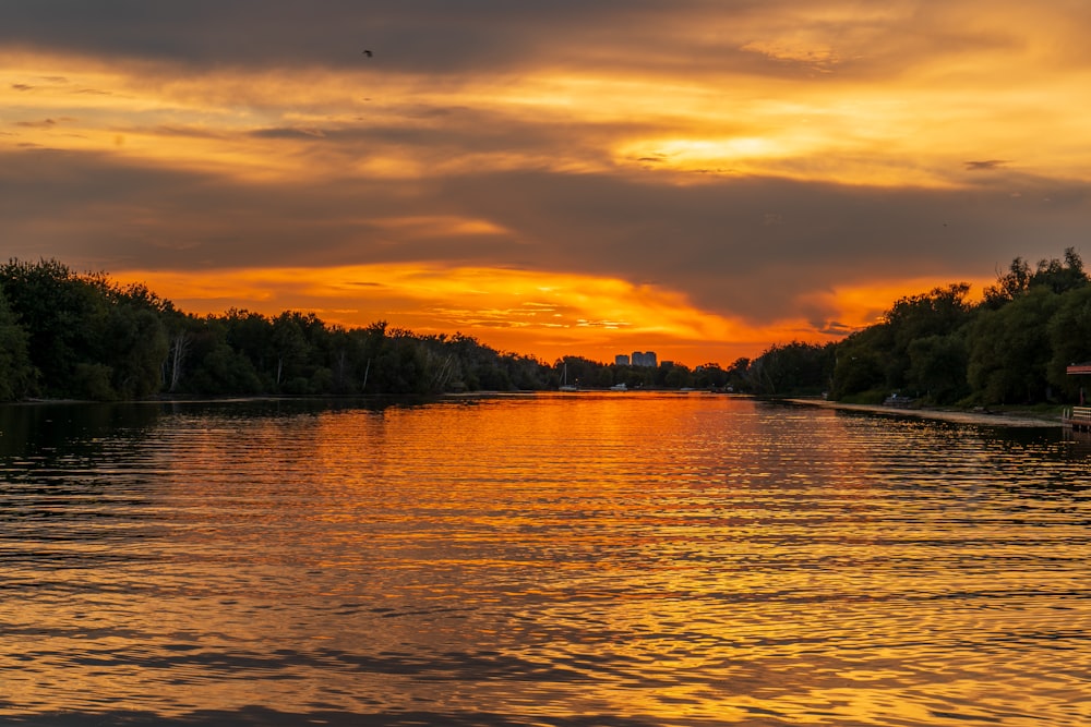 a body of water with trees and a sunset in the background