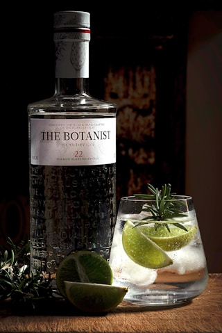 a bottle of alcohol next to a glass of liquid and limes