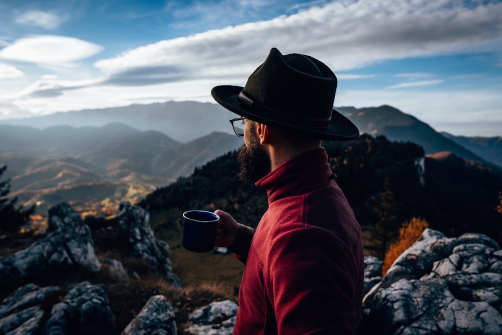 Un hombre con un sombrero y una taza de café en una montaña