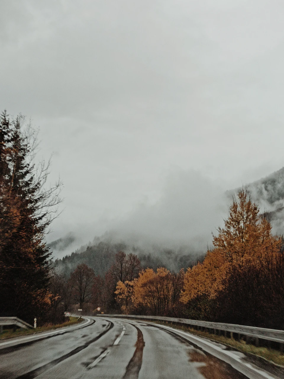 Winding road through mountains with trees on either side under foggy mountain range background