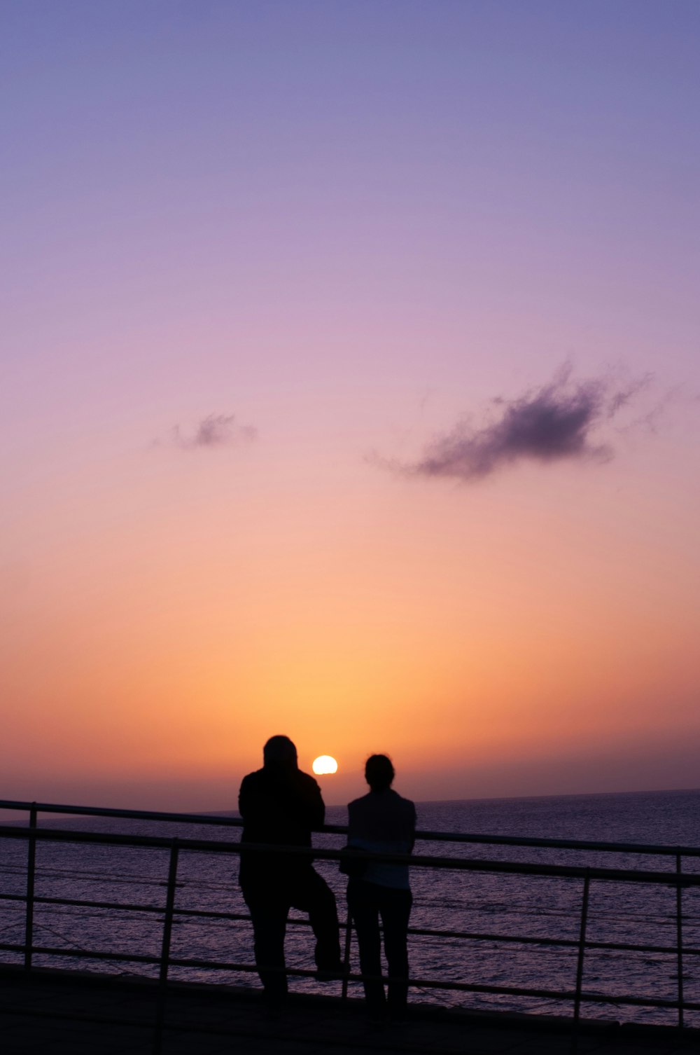 a couple of people standing on a pier looking at the sunset