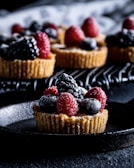 A vibrant berry tart topped with glossy strawberries and blueberries, set against a soft pastel background.