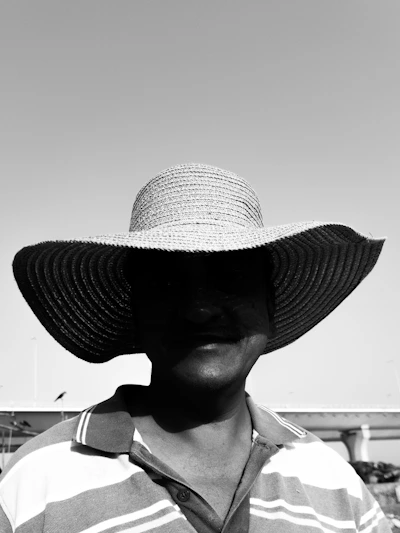 A stylish, wide-brimmed sun hat casting a cool shadow over a smiling face on a sunny city street.