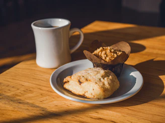 A steaming cup of tea beside a plate of warm muffins on a cozy wooden table.