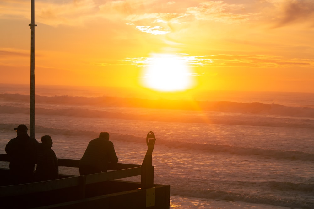 people sitting on a bench looking at the sunset