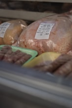A selection of packaged poultry displayed in a refrigerated case, including a whole chicken with a label indicating it is free-range. Sausages are placed on trays nearby.