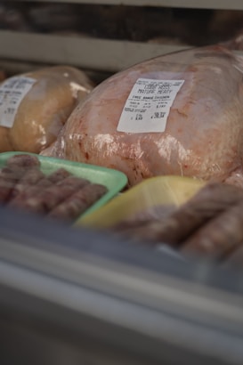 A selection of packaged poultry displayed in a refrigerated case, including a whole chicken with a label indicating it is free-range. Sausages are placed on trays nearby.