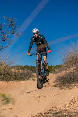 A cyclist using a handheld smart pump with digital pressure display on a sunny trail.