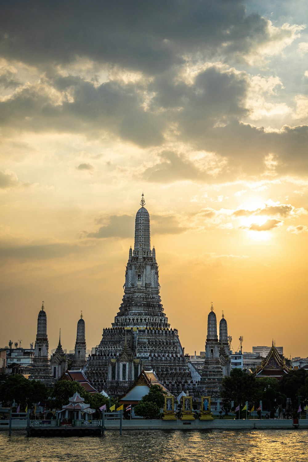 a large building with towers by a body of water with Wat Arun in the background