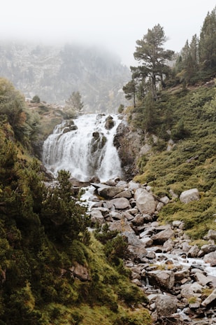 Panoramic shot of a waterfall nestled in the hills of Purwakarta with mist rising around the rocks.