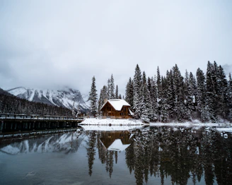 a cabin on a lake surrounded by snow covered trees