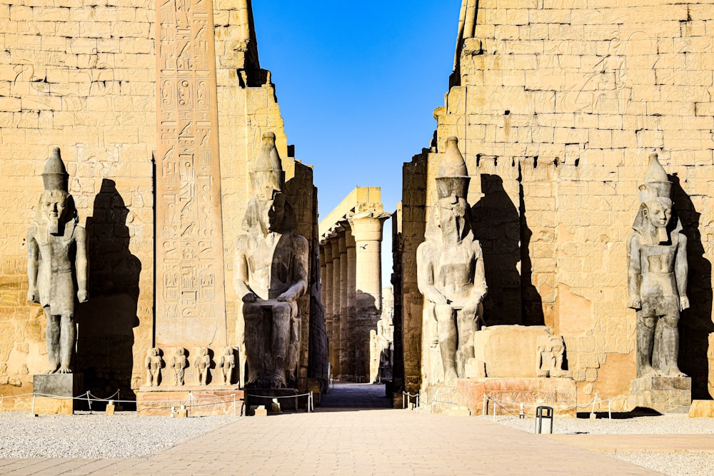 a group of statues in a large stone building with Luxor Temple in the background