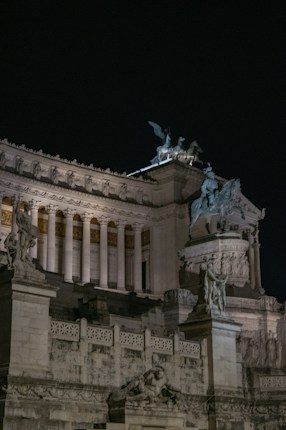 A neoclassical architectural structure featuring ornate sculptures and grand columns, illuminated under the night sky.