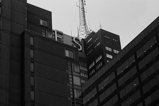 A black and white photograph of tall, rectangular buildings with square windows and a large rooftop antenna. The word 'LIES' is partially visible in large letters on the side of one building.