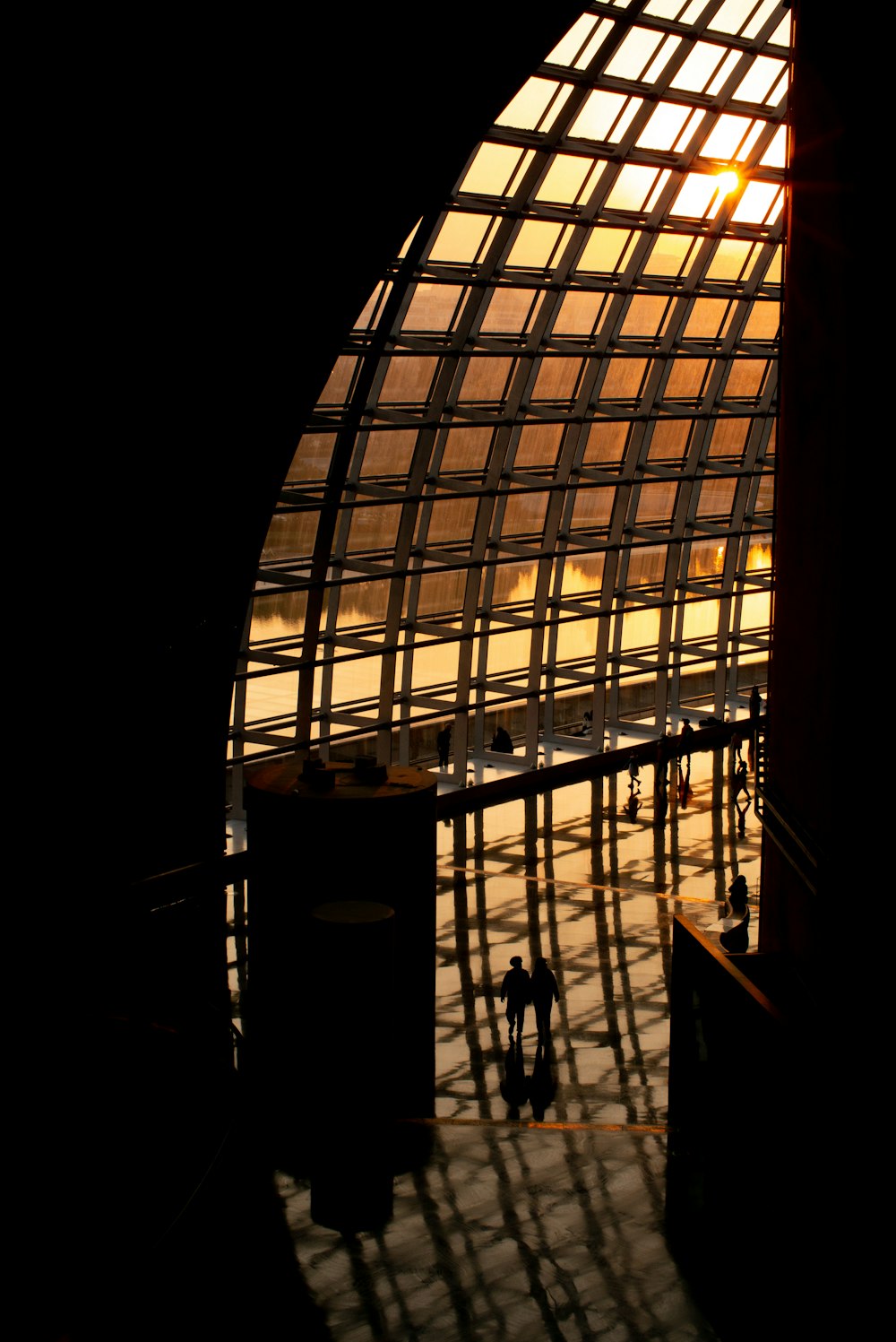 a group of people walking on a walkway between large windows